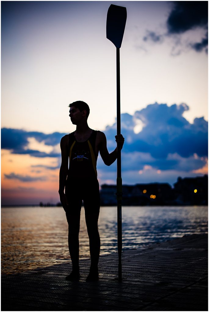 dark picture of man standing by the water holding his rowing oar