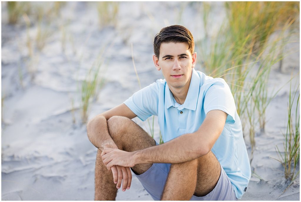 young man sitting in sand dunes for senior pictures